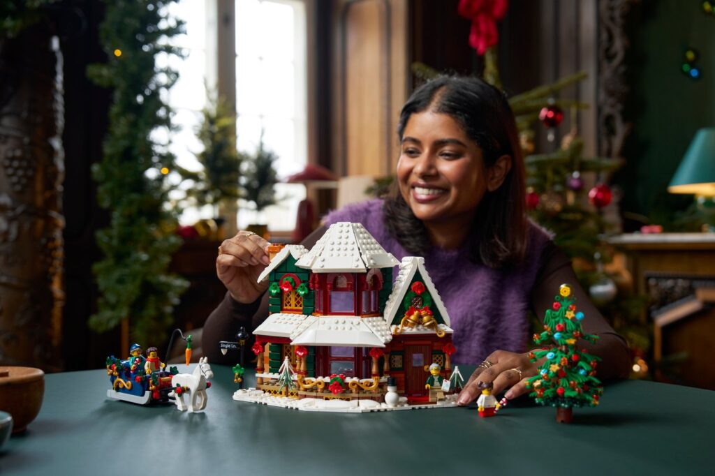 A woman smiling as she finishes the LEGO Holiday House, a snowy red and white house with a sleigh and a Christmas tree