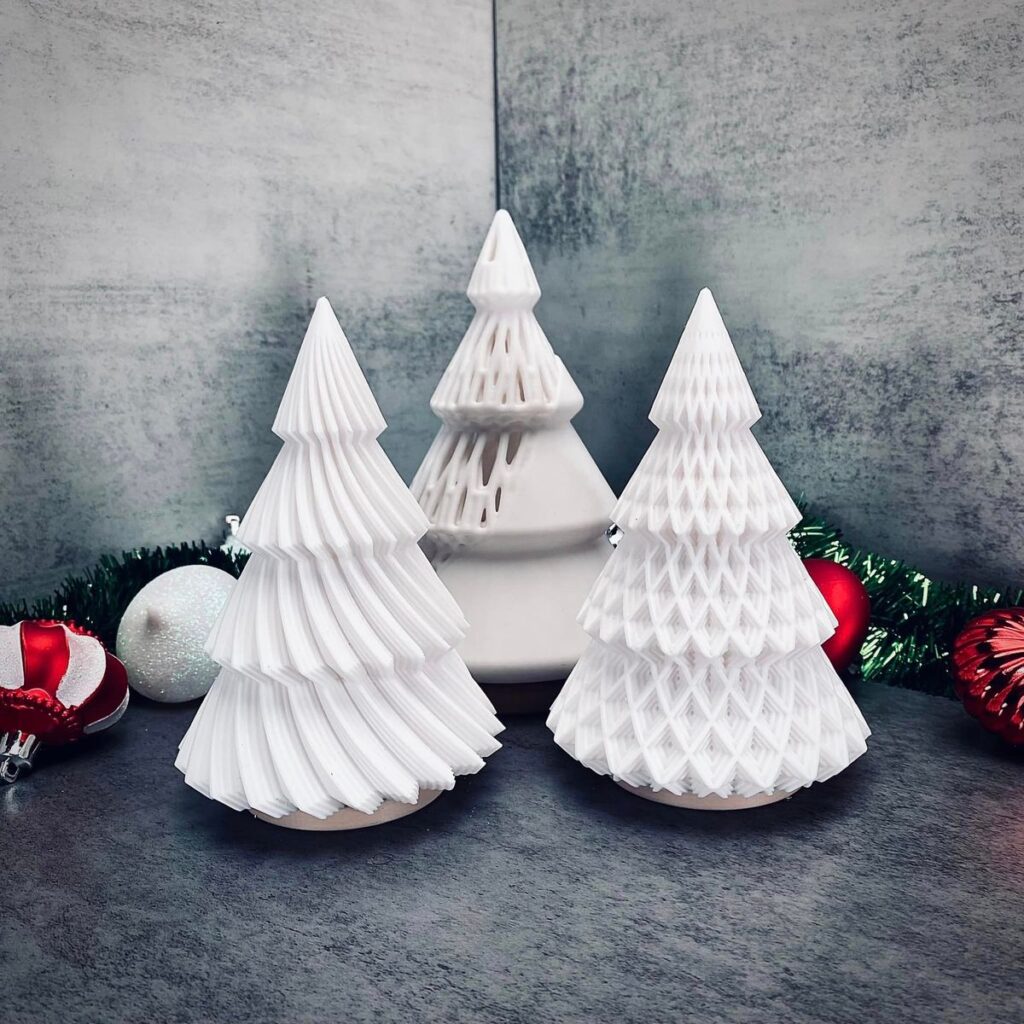 Three white 3D-printed Christmas tree tealight holders with different patterns, with red and white baubles around them