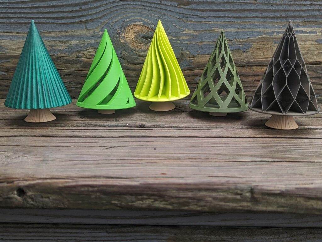 Five small 3D-printed Christmas trees with different patterns, four in shades of green and one in dark grey, on brown printed trunks